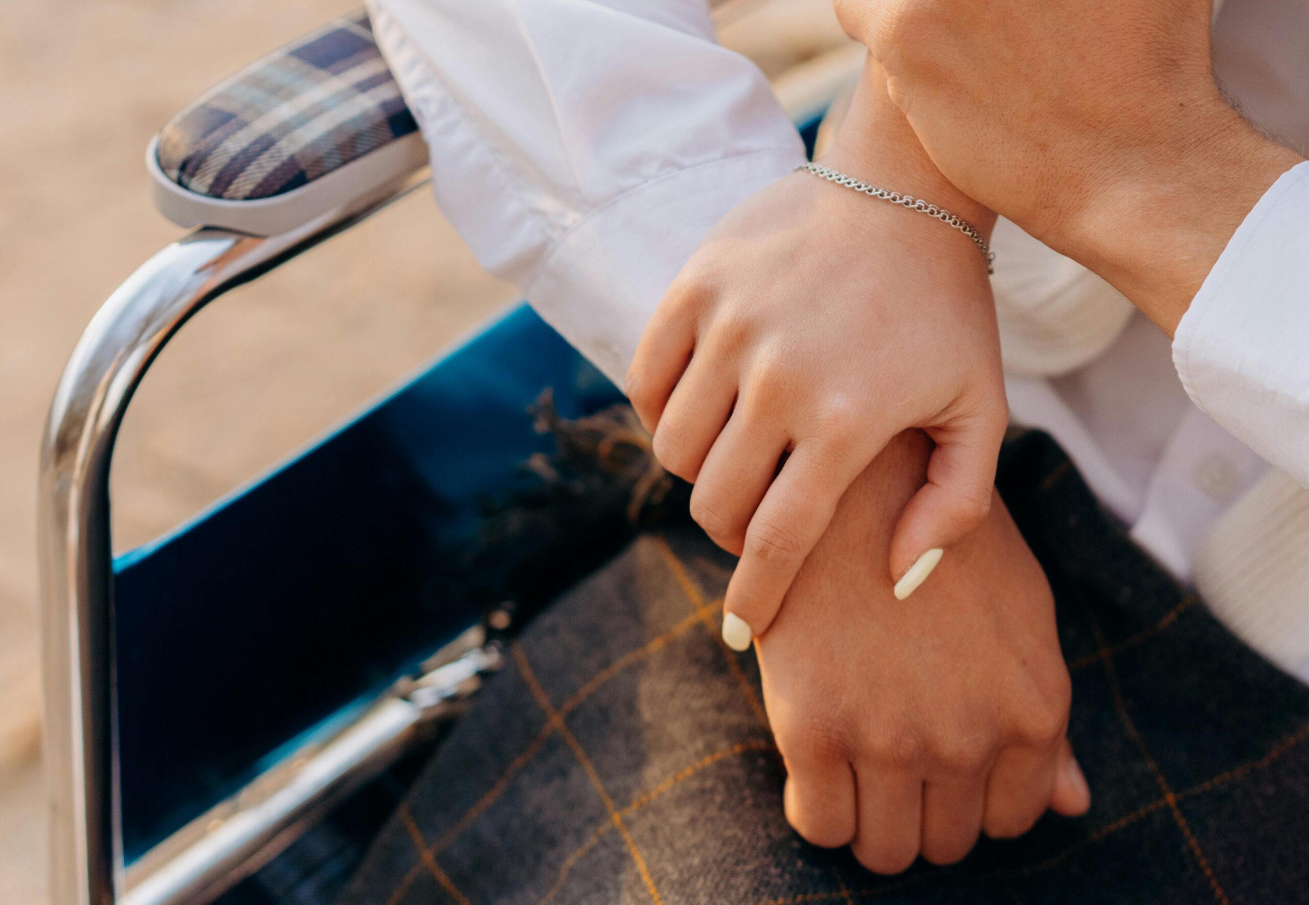 Hands touching each other as a person sits in a wheelchair