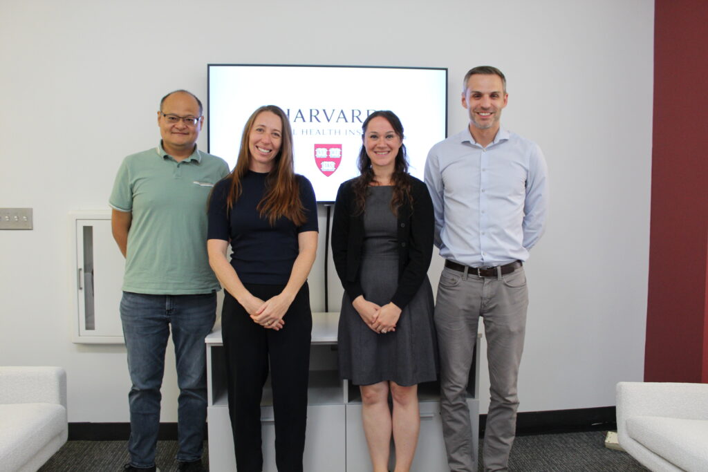 4 Fellows standing by the HGHI logo on the tv screen