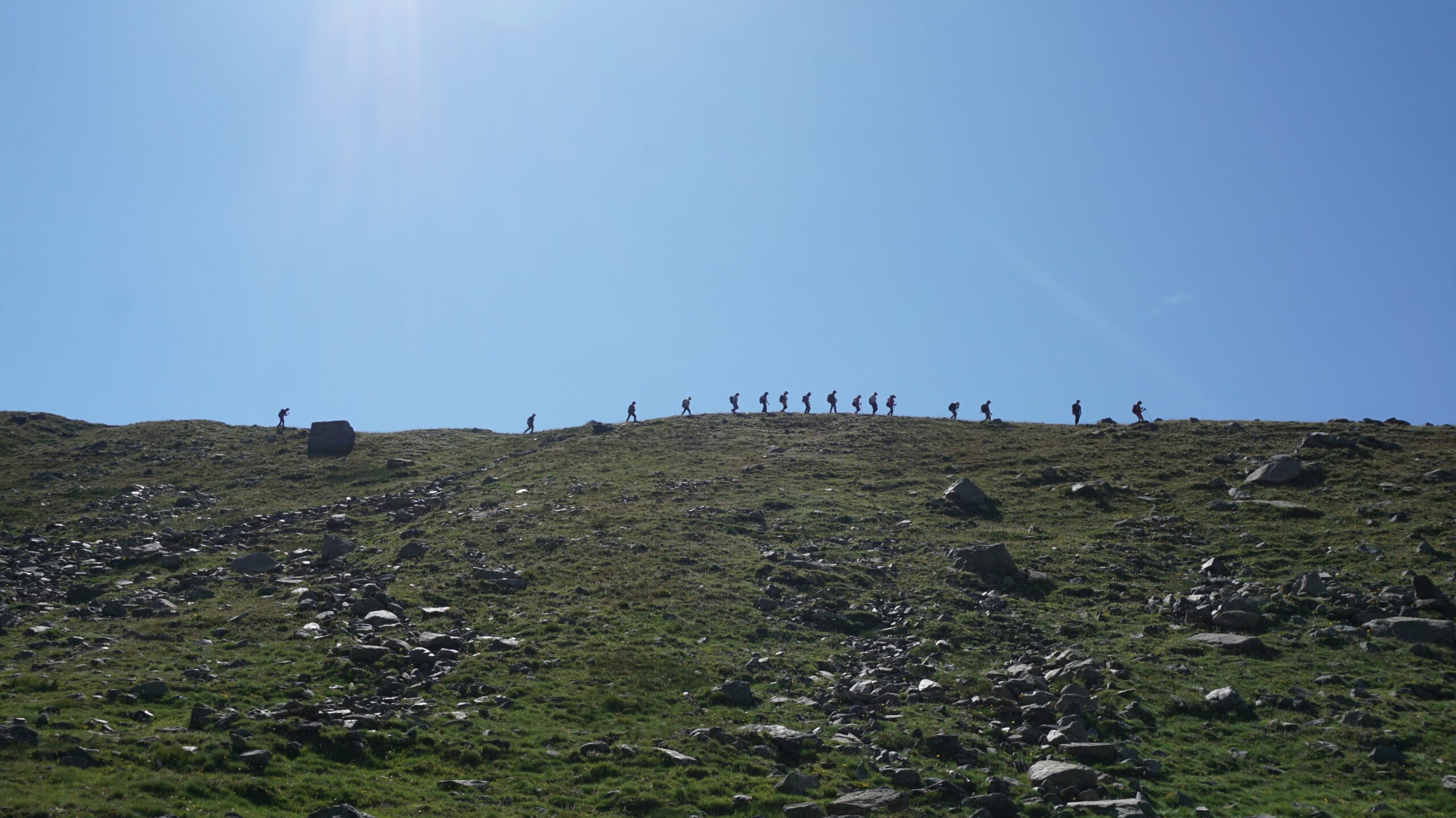 A Hill with a lot of greenery and the bright blue ski above as students trek along.