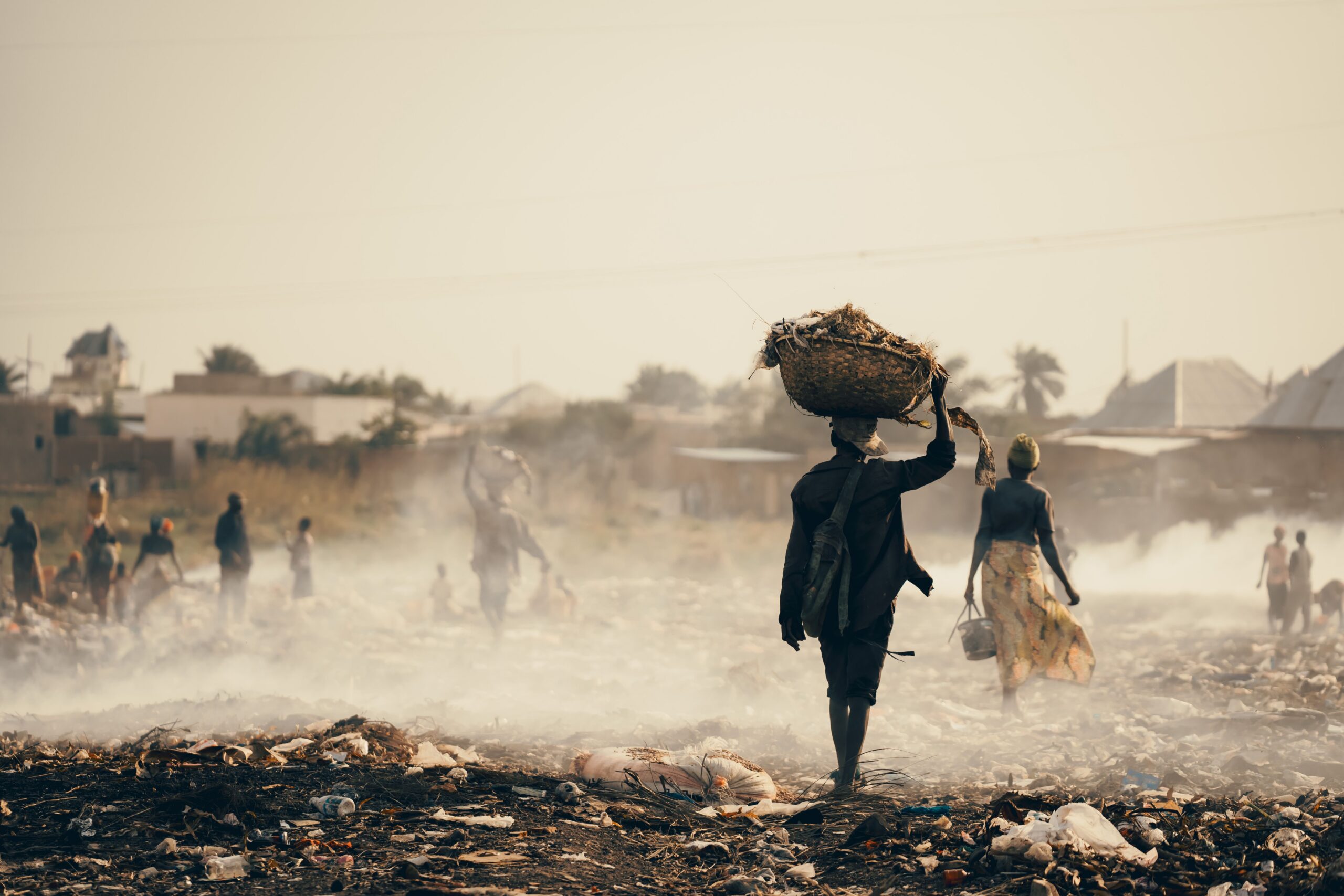 People walk through waste in a smoke-filled landscape in Burundi, highlighting pollution