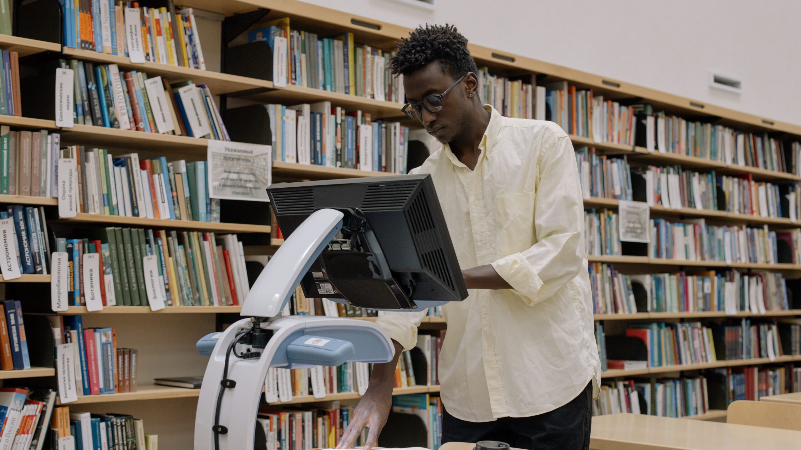 A man scanning books in a modern public library surrounded by bookshelves.